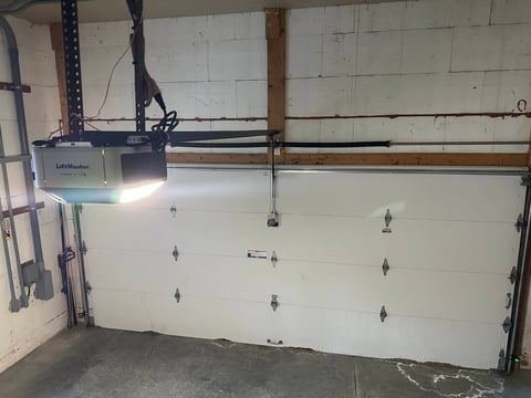 A garage door opener mounted above a white sectional garage door with hardware visible