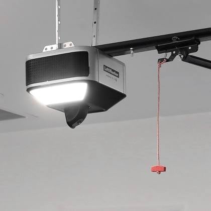 Garage door opener with illuminated light and red emergency release cord mounted on ceiling