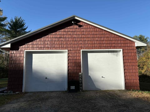 Two-car garage with two white overhead doors and dark roof trim against clear blue sky