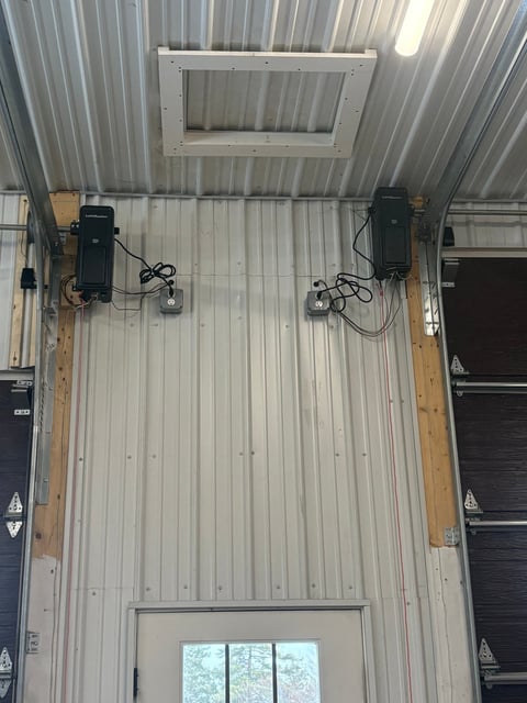 Overhead view of industrial warehouse interior with corrugated metal ceiling, two black heating units mounted on wooden beams, and windows below