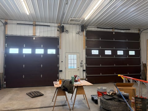 Interior of a garage workshop with two dark garage doors, workbench, tools, and storage materials on a concrete floor