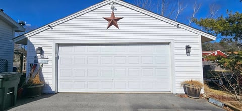 White residential garage with large white door and decorative rust-colored star under the gable roof on a clear day