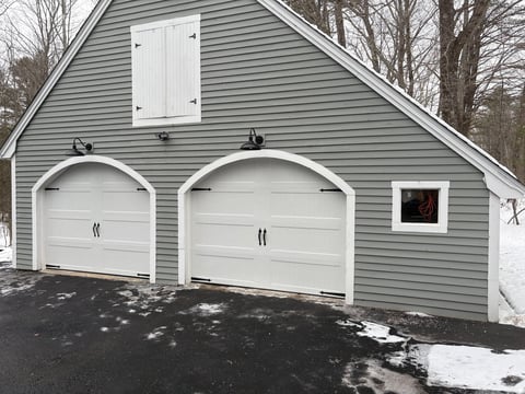 Two-car white garage with horizontal siding, arched doors, and small upper window on residential driveway