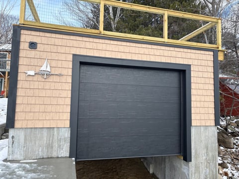 Modern garage structure with tan shingle siding, dark garage door, and yellow-trimmed clerestory windows above